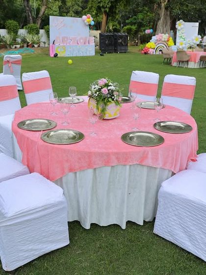A closer look at a guest table at the outdoor sunshine party. The pink tablecloth and white chair covers with coral sashes create a bright and happy color scheme.