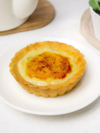A classic crème brûlée tart with a perfectly caramelized sugar top. The bright, natural light highlights the glossy surface, making it an ideal shot for a bakery or cafe menu.