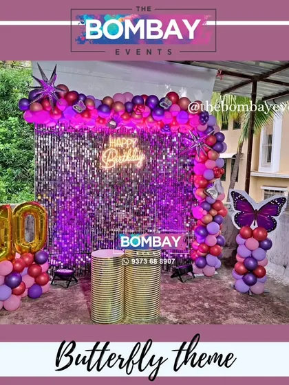 A vibrant butterfly theme for a 10th birthday. This outdoor setup uses a purple sequin wall, a balloon arch in shades of purple and pink, and a large butterfly cutout.