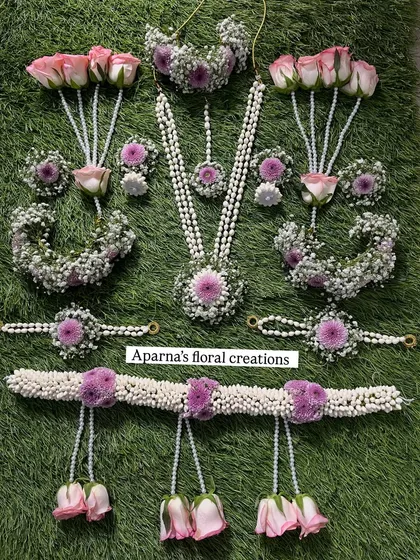 Here is a full baby shower jewellery set, laid out to show every detail. It includes a long necklace, choker, maang tikka, earrings, haath phool, and a kamarband (waistband), all made from fresh pink roses, purple flowers, and fragrant jasmine buds.
