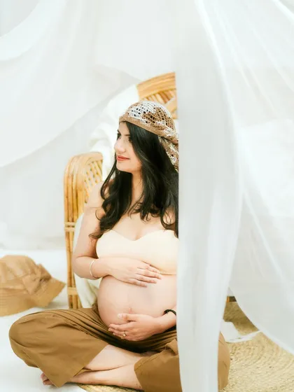 A beautifully framed shot using flowing white curtains. This adds a layer of depth and artistry to the solo maternity portrait.
