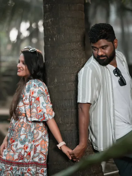 A playful pre-wedding pose with the couple holding hands around a tree trunk, sharing a sweet, stolen glance.