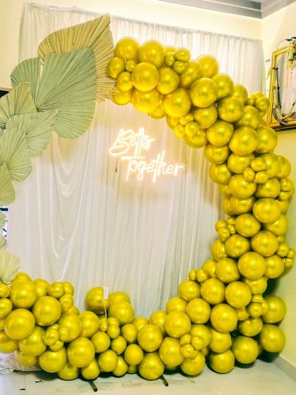 This unique balloon ring arch uses all-gold balloons and dried palm leaves for a modern, bohemian look. The "Better Together" neon sign makes it suitable for anniversaries or birthdays.