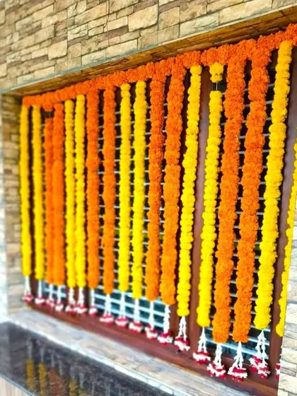 A window decoration for a housewarming using strings of orange and yellow marigolds. This is a simple way to add a traditional festive look.