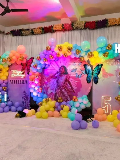 A vibrant and colorful butterfly-themed 5th birthday party. This stage setup includes a multi-panel backdrop, a rainbow balloon arch, and large butterfly cutouts for a whimsical feel.