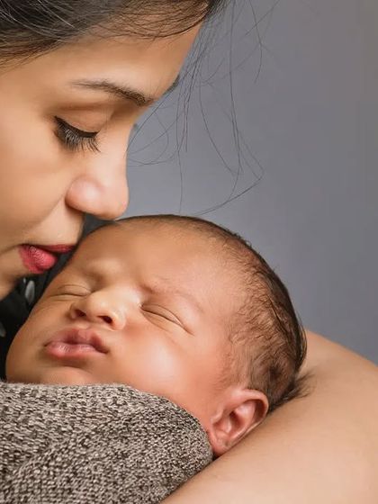 A mother gently kisses her sleeping newborn's forehead. These close-up shots with parents highlight the tender, protective love of the first few weeks.