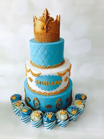 A cake fit for royalty. This grand, three-tiered prince-themed cake in blue and gold, complete with a crown topper and matching cupcakes, is designed to make your little one feel like a king on his birthday.