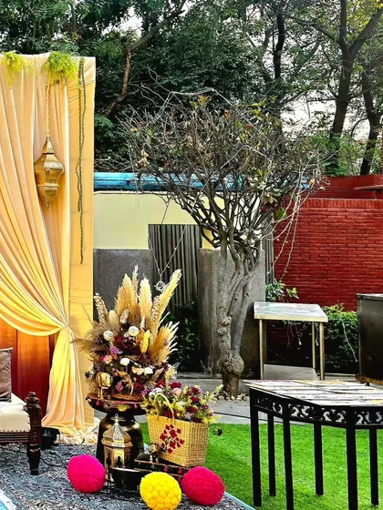 A corner of the Sangeet venue, showing how I blend natural elements with decor. A beautiful floral arrangement with pampas grass stands next to a tree, complemented by colorful fabric spheres on the ground.