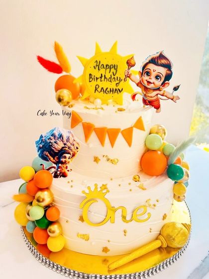 Celebrating the spirit of Bal Hanuman with this vibrant two-tier cake, complete with his Gada and other divine elements.