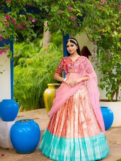 A full-length shot of a designer half saree, set against vibrant blue pots and bougainvillea. The colorful background makes this traditional look feel modern and fresh.
