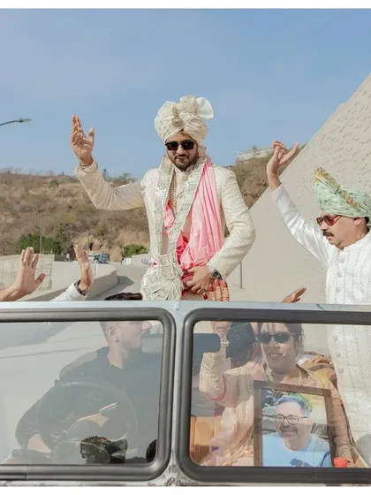The groom's grand entrance in a vintage car. His joyful wave and stylish sunglasses capture the celebratory mood of the baraat.