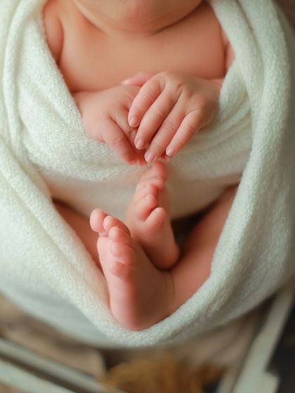 A close-up macro shot focusing on the delicate details of a newborn's hands and feet, snugly tucked inside a white swaddle. These are the tiny features you'll want to remember forever.