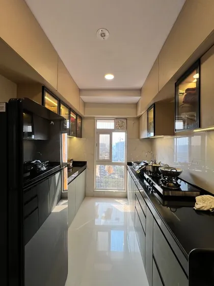 A sleek parallel kitchen with a black countertop and glossy beige and grey cabinets. The layout maximizes efficiency in a compact space.