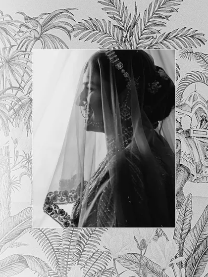A serene black and white profile of the bride, with her face gently veiled. This artistic shot highlights her traditional nath (nose ring) and the delicate embroidery on her dupatta.