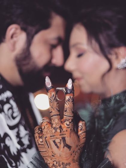 A close-up and personal shot focusing on the bride's mehndi-adorned hand and the couple's rings. The intimate embrace in the background makes this a very romantic and detailed photo.