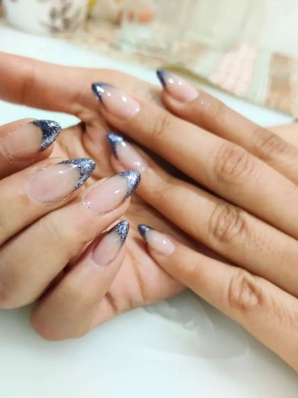 A glamorous French manicure with a deep blue glitter tip on long, almond-shaped gel extensions for a sparkling, dramatic effect.