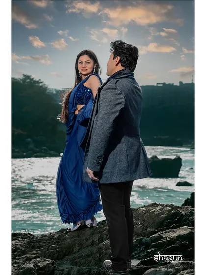 A dramatic pose on the rocks by the river. The bride's vibrant blue saree stands out beautifully against the water and the evening sky, creating a stunning and colorful portrait.