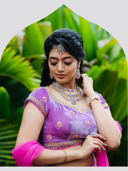 The model adjusts her jewelry, giving a better view of the neckline and embroidery on the velvet blouse. The ensemble is designed for elegance and poise.