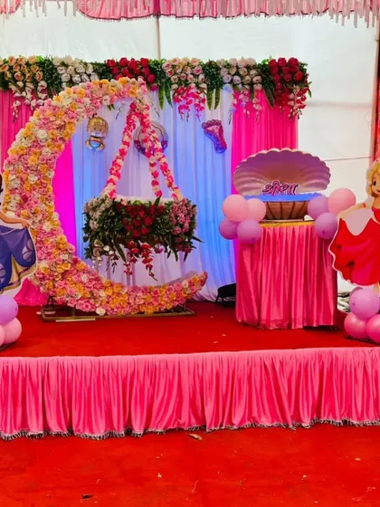 A princess-themed naming ceremony. The stage features a floral crescent moon holding the jhula, with cutouts of Disney princesses on either side.
