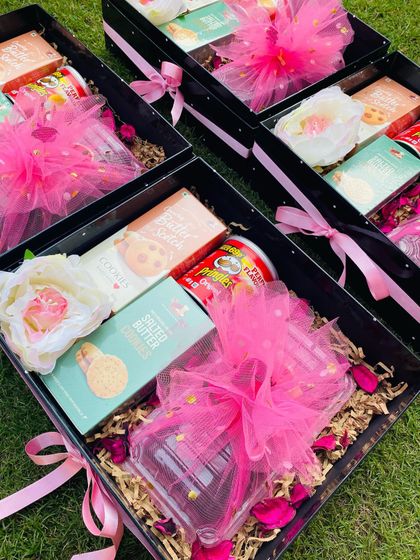 An array of custom Diwali gift boxes, each containing a delightful mix of sweet and savory snacks. The vibrant pink tulle wrapping adds a touch of festive cheer.