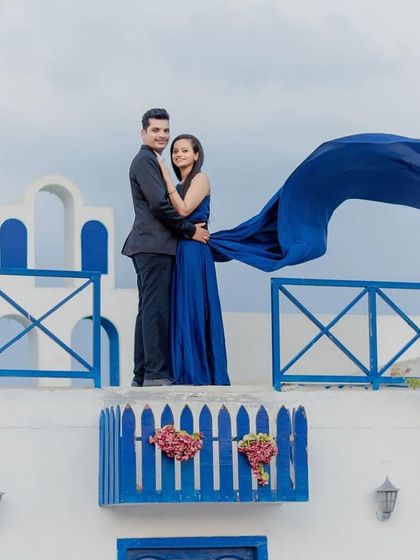A beautiful shot on a Santorini-style balcony, with a flowing blue dress catching the wind to create a dynamic and romantic image.