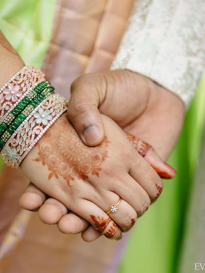 A close-up on the couple's hands, highlighting the bride's engagement ring, henna, and colorful bangles.
