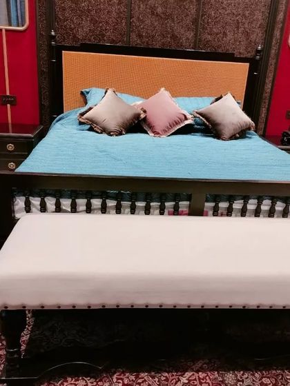 A classic four-poster bed with a twist. This design uses dark, turned-wood posts and a natural cane headboard, paired with a simple white upholstered bench at the foot of the bed.