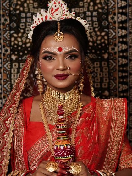 A front-facing portrait of the Bengali bride, showing the intricate gold-plated choker and the traditional headwear in detail.