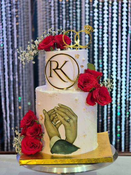 A beautiful two-tier engagement cake featuring fresh red roses, a custom 'RK' monogram, and a unique edible image of the couple's hands. I love adding these personal details that tell a story.