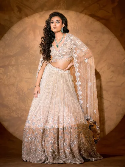 Ethereal elegance brought to life. This full-length shot showcases the delicate craftsmanship of a silver and beige lehenga, using soft lighting to create a dreamy, romantic mood perfect for a luxury lookbook.