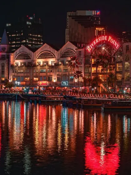 The "Riverside Point" sign glows in red neon at Clarke Quay, with the colorful buildings reflecting beautifully in the water.