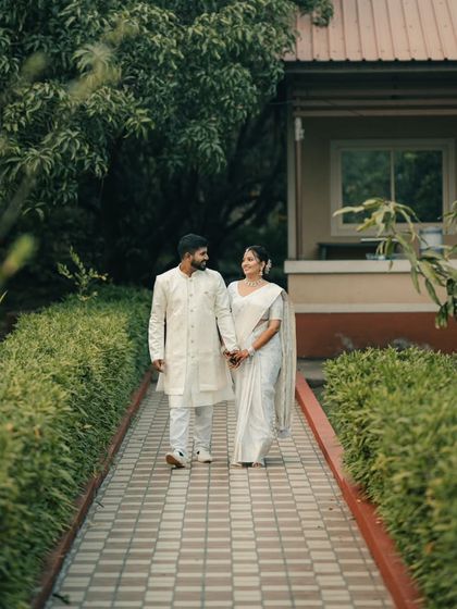 A full-length shot of the couple walking along a path, showcasing their coordinated white outfits against the backdrop of a resort-like setting.