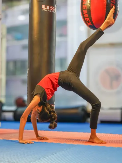 A student executes a graceful bridge pose, lifting one leg to touch a stability ball. This drill improves back flexibility, core strength, and body awareness, key elements in artistic gymnastics.