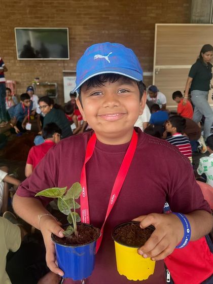 A smiling camper proudly holds up his newly potted plants. Our goal is to make learning about agriculture a joyful and rewarding experience.