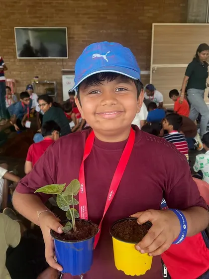 A smiling boy holds up the two plants he potted during our 2024 summer camp. Taking home a plant they've potted themselves is a highlight for many of our young visitors.