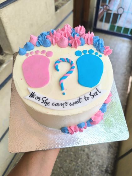 "He or She, can't wait to see." This cute gender reveal cake features pink and blue baby footprints and piped buttercream swirls to build the anticipation.
