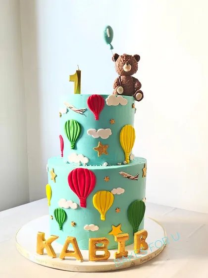 A charming two-tier hot air balloon cake for a first birthday. This design features a cute teddy bear, fluffy clouds, and colorful balloons for a gentle and dreamy theme.
