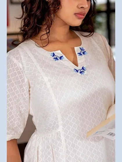 This close-up on a white textured top focuses on the delicate blue floral embroidery around the neckline. It's a perfect shot for product pages where customers want to see the quality and craftsmanship up close.