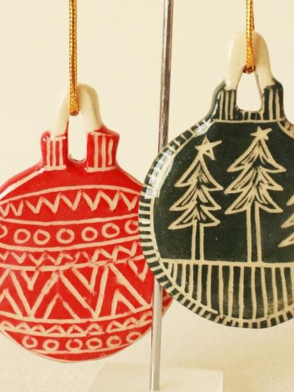 A pair of red and green ornaments with carved tribal and forest patterns. The contrast between the color and the revealed white clay makes the designs pop.
