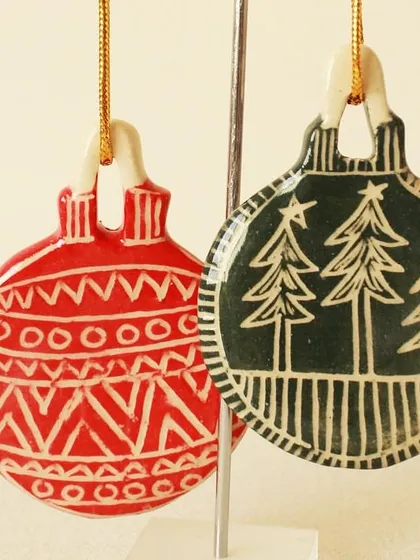 A pair of red and green ornaments with carved tribal and forest patterns. The contrast between the color and the revealed white clay makes the designs pop.