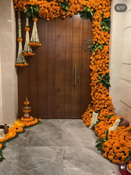 I make your home's entrance feel truly festive and welcoming. This traditional doorway decoration features dense garlands of fresh orange marigolds, accented with hanging jasmine tassels and a floral rangoli, setting a perfect tone for any celebration like Diwali or a housewarming pooja.