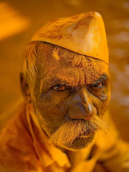 An intense, close-up portrait of a man at the Pattan Kodoli festival, his face and mustache completely covered in yellow turmeric. His direct gaze is powerful and unforgettable.