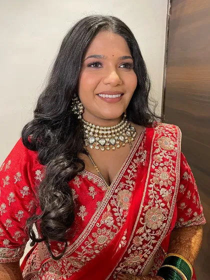 A happy bride in her vibrant red embroidered saree. The makeup is kept fresh and glowing, with a focus on her radiant smile.