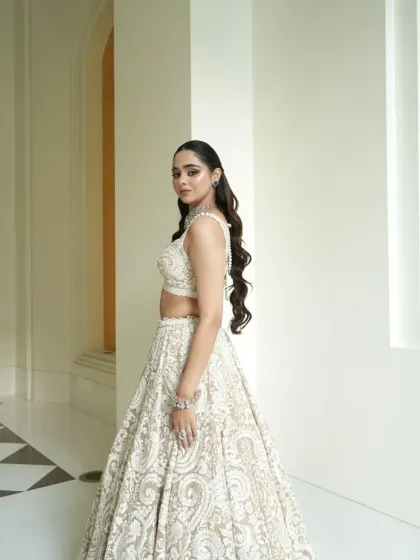 A side profile that highlights the intricate texture of the lehenga and the bride's elegant, wavy hairstyle.