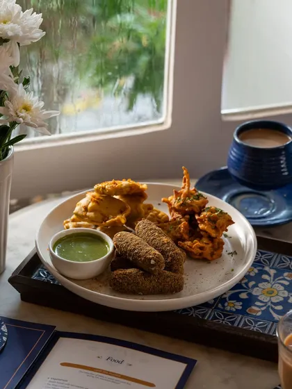A still life of the pakora platter and chai, set against a rainy window for a cozy, monsoon mood.