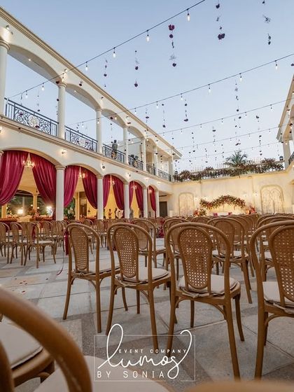 A stunning view of a regal wedding setup within a grand courtyard. The architecture is complemented by rich red drapes and elegant seating, setting the stage for a royal affair.