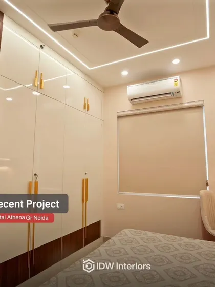 This bedroom design focuses on maximizing storage with sleek, glossy white and wood wardrobes featuring stylish gold handles.