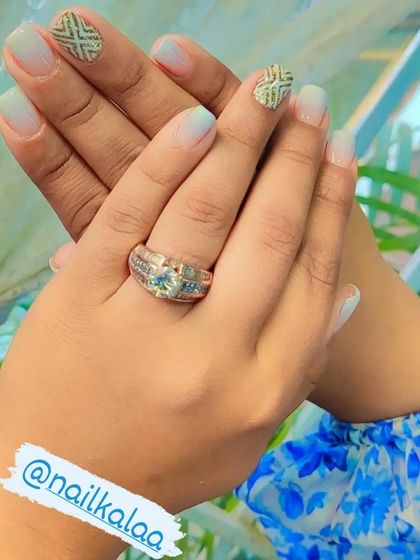 A soft baby blue ombre on natural nails, with accent nails featuring a textured gold geometric pattern.