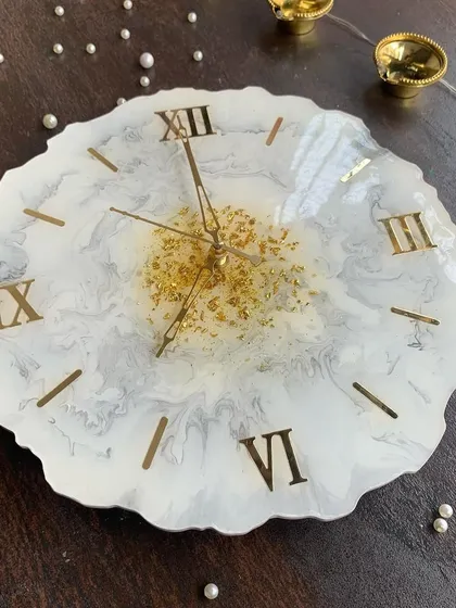 An elegant clock with a free-form shape, featuring a white and grey marble effect with a splash of gold leaf in the center.