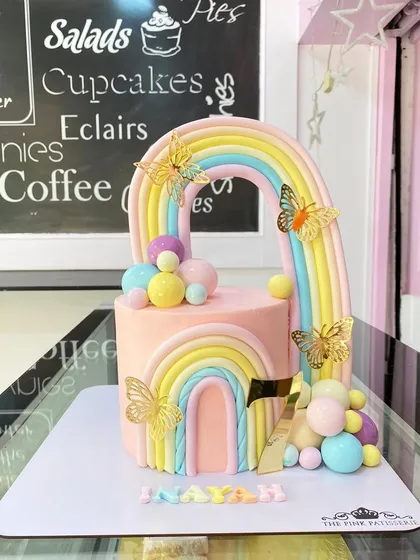 A vibrant rainbow and butterfly cake. This design features a double rainbow arch, pastel-colored spheres, and delicate golden butterflies for a magical touch.